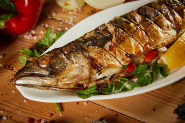 Appetizing grilled fish with vegetables on wooden background. Homemade smoked mackerel fish. Appetizing scomber prepared on tandoor (barbecue) on a brown rustic wooden table.