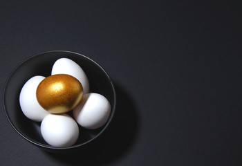 Easter attributes golden and white eggs lie in a black plate. The plate is on a black background. trend black monochrome