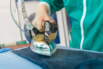 Female hand ironing blue jeans in a dry cleaning  service