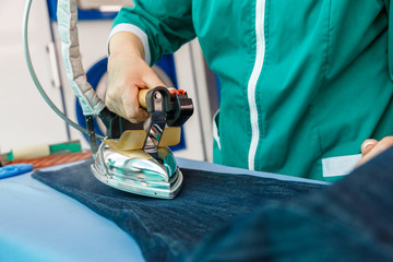 Female hand ironing blue jeans in a dry cleaning  service