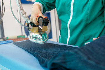 Female hand ironing blue jeans in a dry cleaning  service