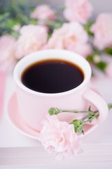 Pink cup of black coffee and pink carnation flowers on a light background