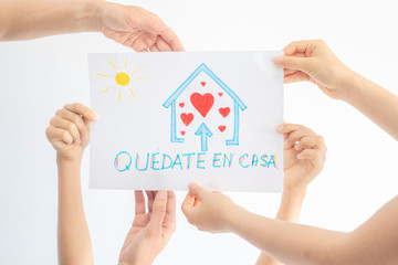 Coronavirus pandemic self quarantine in Spain. Family hands holding kid drawing picture with spanish words Quedate en casa - Stay at home