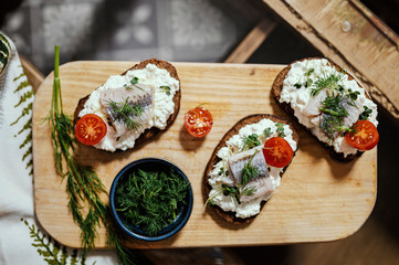 Brown bread with cottage cheese and herring on a wooden plate.