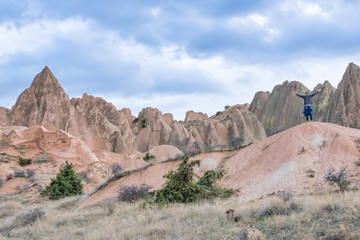Adventurous person with spreaded hands is stadning on the rock and enjoying the panorama of Cappadocia. Travel destination in Turkey.