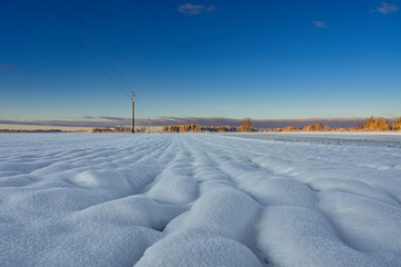 Winter sunrise over snow covered field with round shape snow piles .