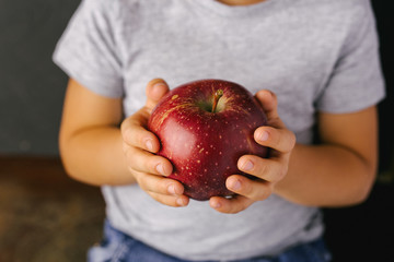 Big red apple in the hands of a boy, a sign of health