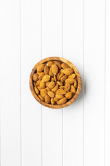 Dried almonds nuts in wooden bowl on white table.