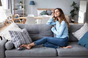 Tranquil smiling millennial woman leaning on sofa.