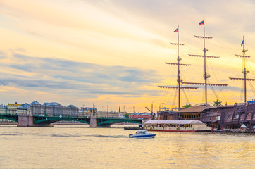 Cityscape of Saint Petersburg Leningrad with bascule Exchange Bridge, sailboat wooden ship with mast moored anchored on water of Neva river, evening dramatic orange sky background, Russia