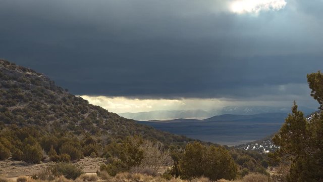 View of sun rays shining through dark clouds moving over the landscape on windy day in the desert.