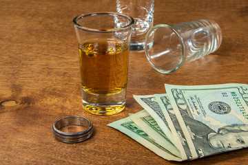 shot of whiskey with wedding ring and money on wood table
