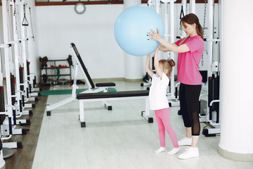 Fototapeta na wymiar Mother with daughter in a gym. Little girl are engaged in gymnastics