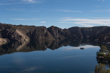 a lake formed by a dam that reflects the sky and barges that run through its calm waters