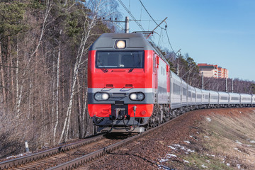 Passenger train approaches to the station at spring day time.