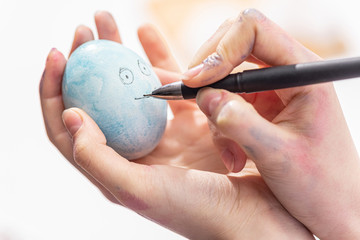 Easter celebration concept. Home tradition of painting eggs. Woman draws with pen on Easter egg. Close-up.