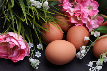 Easter eggs among spring flowers on a black textured background.