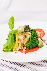 Steamed cod fish fillet with broccoli, tomato, lemon, avocado, basil sauce and pine nuts on a white background. Copy space