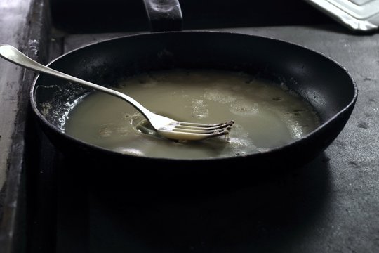 dirty frying dripping pan with used fat and fork