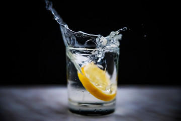 Splash in a glass with lemon on a black background. Fresh healthy drink concept