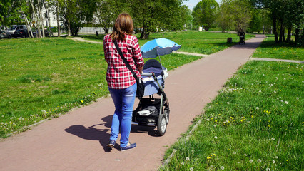 Fototapeta Mama z nowo narodzonym dzieckiem w wózku. Kobieta spaceruje w parku blisko lasu. Dziecko na świeżym powietrzu, dbanie o zdrowie dziecka. Noworodek śpi na spacerze. Urlop macierzyński. Słoneczny dzień. obraz