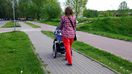 Mama z nowo narodzonym dzieckiem w wózku. Kobieta spaceruje w parku blisko lasu. Dziecko na świeżym powietrzu, dbanie o zdrowie dziecka. Noworodek śpi na spacerze. Urlop macierzyński. Słoneczny dzień.
