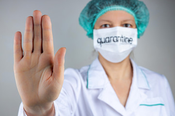 A doctor in a medical mask with the inscription quarantine shows a stop sign with his palm on the COVID 19 epidemic, close-up, shallow depth of field, selective focus. The concept of quarantine