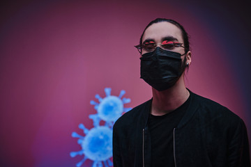 Young adult caucasian man wearing black clothes, sunglasses and medical mask, posing in a studio with calm face, in front of coronavirus background
