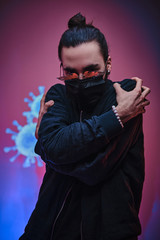 Young adult man wearing medical mask, sunglasses and black clothes looking scared and terrified of coronavirus. Isolated in a bright studio, vertical portrait