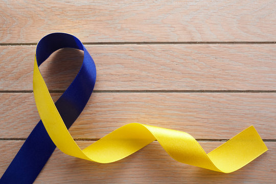 Blue and yellow ribbon on wooden background. World down syndrome day. Awareness ribbon.