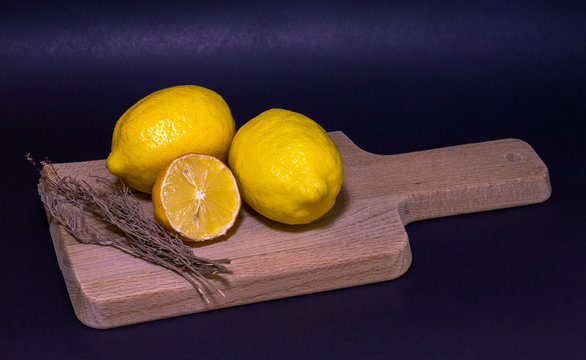 Limones frescos con junto a ramas de romero sobre una tabla de madera y fondo oscuro.