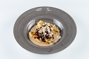 Caramelized and grilled bananas with peanut butter sauce, chocolate syrup and nuts isolated on white