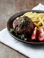 Hamburger steak with french fries and tomatoes. Brown stone background