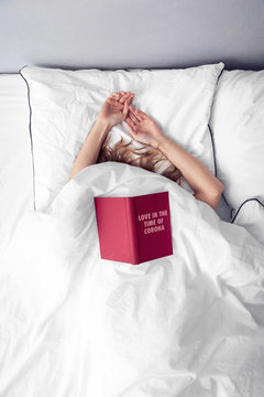 Frau mit Buch Love in the Time of Corona im Bett