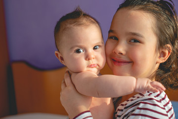 Big little sister holding her little sister and looking at camera.