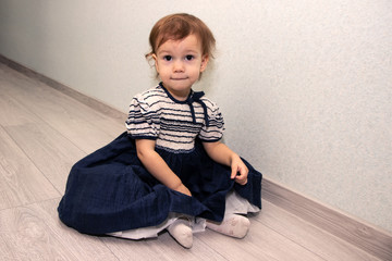 a little girl in a dress sitting on the floor