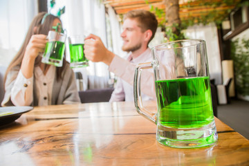 The company of young people celebrate St. Patrick's Day. They have fun at the bar. They are dressed in carnival headgear