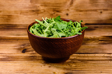 Ceramic bowl with arugula leaves on wooden table