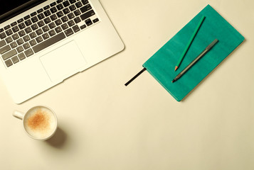 Work space with laptop, turquoise notebook and cinnamon coffee on white table. Flat lay, top view