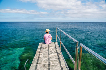 Fototapeta premium A man with a hat, tourist, in summer, enjoys the view of the sea from a stone walk on the coast