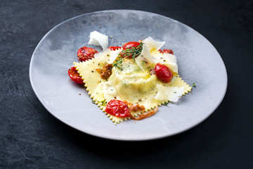 Traditional Italien ravioli pasta offered with parmesan cheese and fried tomatoes as closeup on a modern design plate