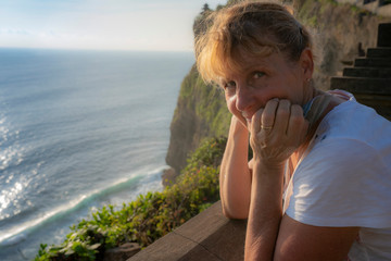 In the golden light of the setting sun, a woman pauses for a portrait photo on the Uluwatu temple...