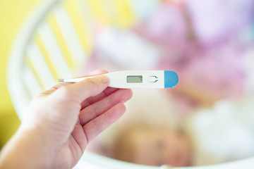 Close-up medical thermometer, Parent measuring temperature of ill kid, 1 years old toddler girl gets high fever lying on bed. fever in child