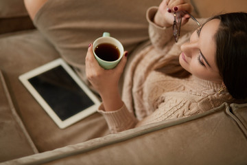 Happy young woman sitting on sofa holding a mug at home in the living room