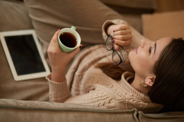 Happy young woman sitting on sofa holding a mug at home in the living room