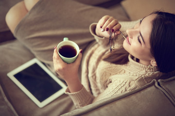 Happy young woman sitting on sofa holding a mug at home in the living room