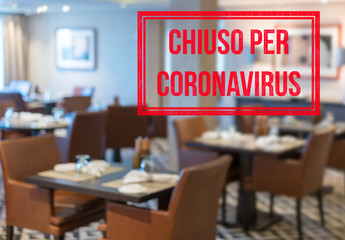 Defocused view of interior of an upmarket restaurant empty and closed with Italian notice saying Closed due to Coronavirus