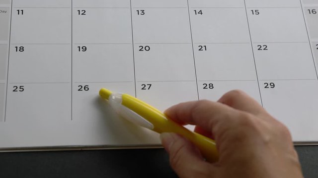 Checking and running through the dates on a table calendar with a pen. Appointment or schedule concept.