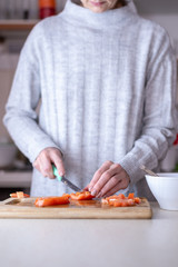 Young female chef in kitchen at home preparing fresh salad slicing tomato and olives on cutting board. Healthy eating