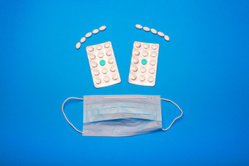 face of a white medical mask and pills on a blue background